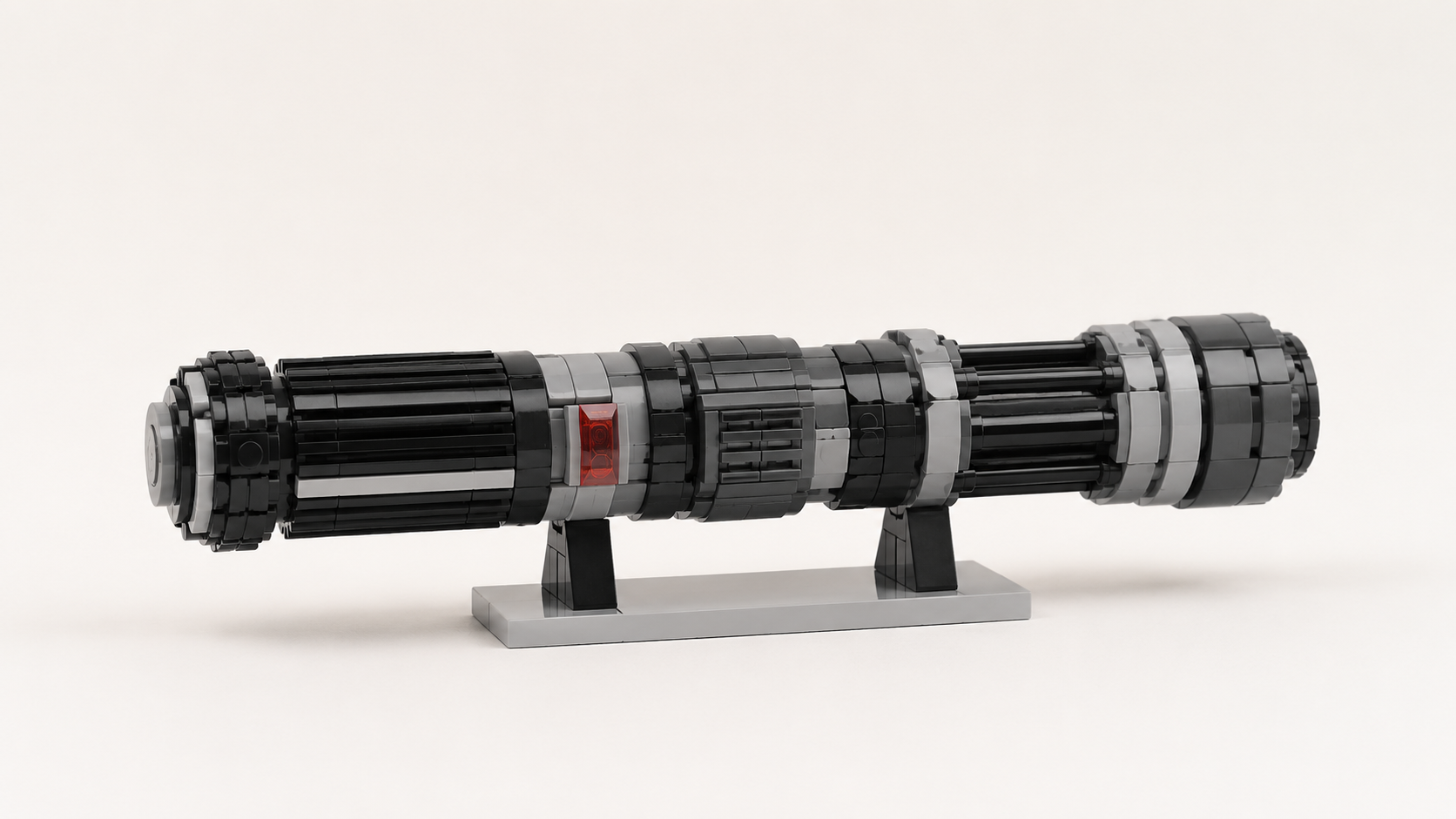 Generyczna klockowa rękojeść sci-fi w czerni i szarościach z małym czerwonym przezroczystym detalem, ustawiona na prostej podstawce na jasnym neutralnym tle.