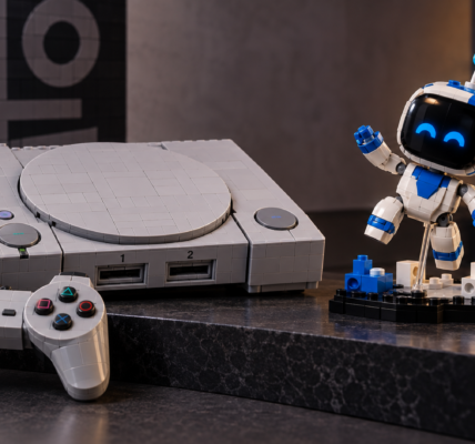 Klockowa konsola w stylu pierwszego PlayStation stoi obok małego biało-niebieskiego robota kolekcjonerskiego na ciemnym blacie.